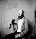 Unknown man in checked coat seated on chair.
